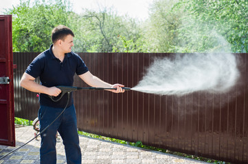 Gun water hose nozzle sprayer. A man's hand holds a black gun watering hose with splash. Man...