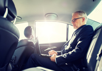 transport, business trip, technology and people concept - senior businessman with laptop computer driving on car back seat