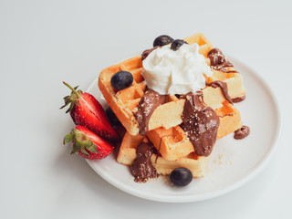 Plate with tasty breakfast. Tasty waffle with fruits, chocolate and whipped cream on a white ceramic plate