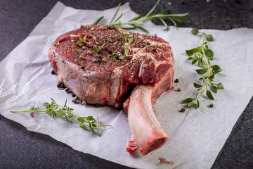 raw tomahawk steak on dark background with spices for grilling