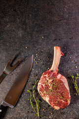 raw tomahawk steak on dark background with spices for grilling
