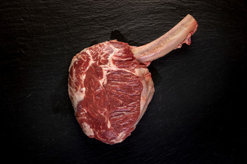 raw tomahawk steak on dark background with spices for grilling