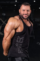 Fototapeta na wymiar Bodybuilder in the gym. Sports photo shoot. Man's fitness. Training and exercises with dumbbells. Men's photo shoot in low key. Athletic build. young man lifting weights in gym