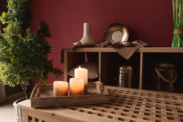 Wicker tray with glowing candles on wooden chest in interior room