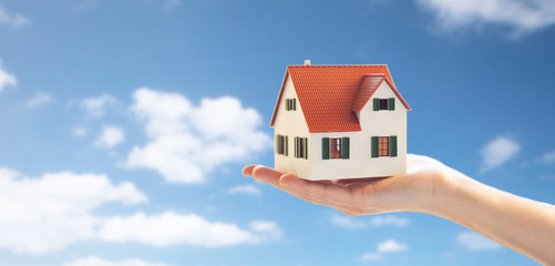 real estate, accommodation and property concept - close up of hand holding house or home model over...
