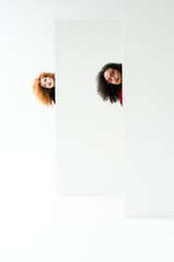 curly redhead girl and beautiful african american woman looking at camera on white