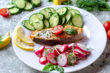 Salmon steak with lemon, tomatoes, cucumber and radish on a plate. Healthy seafood. Proper nutrition food.