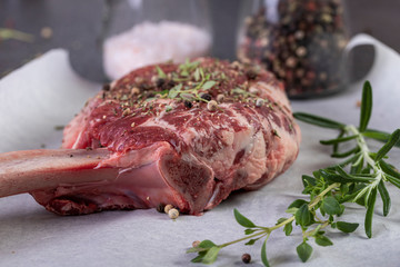 raw tomahawk steak on dark background with spices for grilling