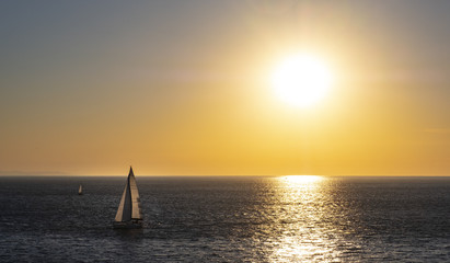 sailboat in the sea with orange light of the sun at sunset