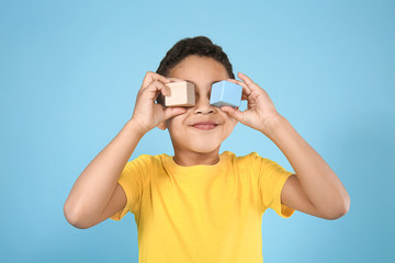 Portrait of cute little boy with cubes on color background