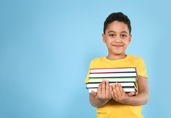 Portrait of cute little boy with books on color background