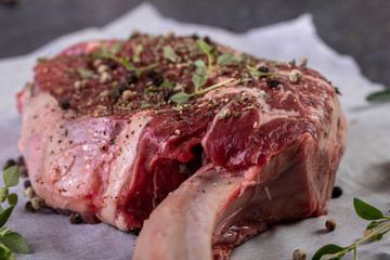 raw tomahawk steak on dark background with spices for grilling