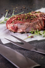 raw tomahawk steak on dark background with spices for grilling