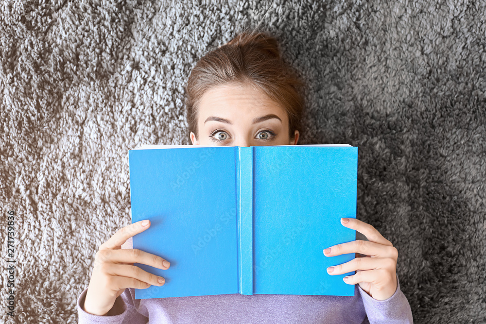 Canvas Prints Surprised young woman with book lying on floor, top view