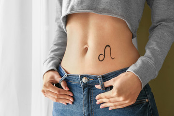 Woman with painted LEO Zodiac sign on her belly indoors