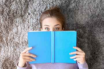 Surprised young woman with book lying on floor, top view