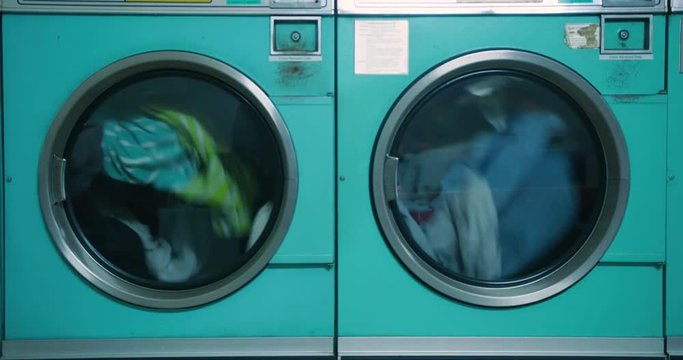 Close Up Two Washing Machines Spinning Clothes At Laundromat