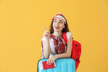 Happy young woman with suitcase, passport and ticket on color background