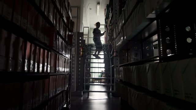 Woman librarian selects the book from a high shelf