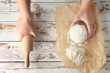 Man with raw dough and rolling pin at kitchen table, top view