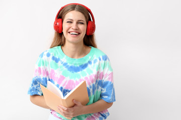 Young woman listening to audiobook on light background