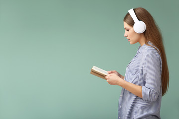 Young woman listening to music and reading book on color background