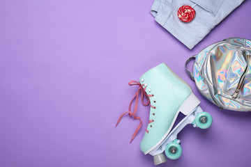 Vintage roller skate, clothes and bag on color background