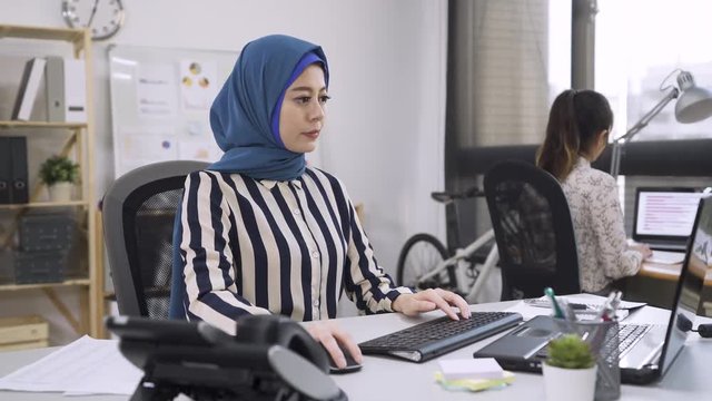 Busy activity in diverse business office with asian people working multitasking in workplace networking with technology. multi ethnic chinese fashion designer with islam colleague typing on computer
