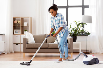 household, housework and cleaning concept - happy african american woman or housewife with vacuum...