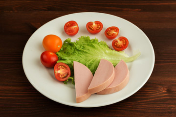 Slices of boiled sausage and lettuce with cherry tomatoes lie on a white plate.
