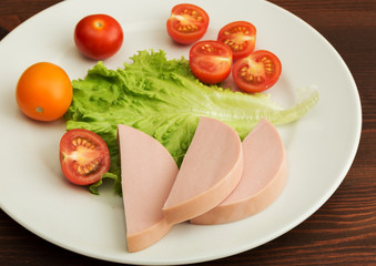 Slices of boiled sausage and lettuce with cherry tomatoes lie on a white plate.
