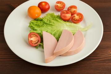 Slices of boiled sausage and lettuce with cherry tomatoes lie on a white plate.