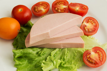 Slices of boiled sausage and lettuce with cherry tomatoes lie on a white plate.