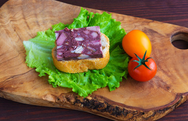 Sandwich with black pudding with a leaf of lettuce and yellow and red tomatoes are on the olive board, natural wood.