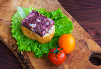 Sandwich with black pudding with a leaf of lettuce and yellow and red tomatoes are on the olive board, natural wood.