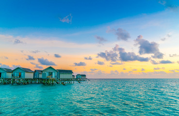 Beautiful water villas in tropical Maldives island at the sunset time .