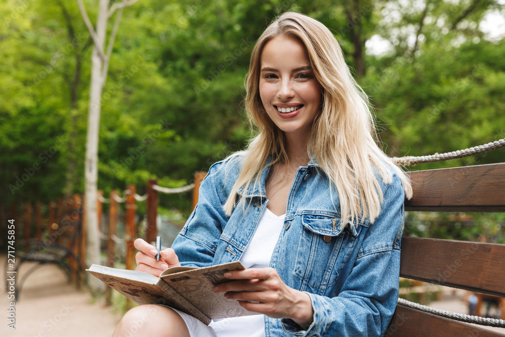 Wall mural amazing happy young woman student posing outdoors in park writing notes in notebook.