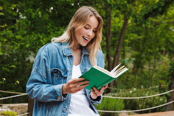 Fototapeta premium Happy young woman student posing outdoors in park reading book.