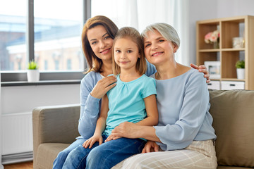 family, generation and female concept - portrait of smiling mother, daughter and grandmother sitting on sofa at home