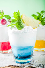 Summer cold drinks. Colorful Italian cream soda cocktails over white wooden background copy space