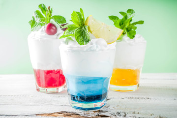 Summer cold drinks. Colorful Italian cream soda cocktails over white wooden background copy space