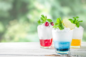 Summer cold drinks. Colorful Italian cream soda cocktails over white wooden background copy space