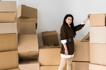 attractive african american woman standing near carton boxes and looking at camera on white