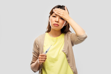 health and fever concept - sick asian young woman with thermometer having headache over grey...