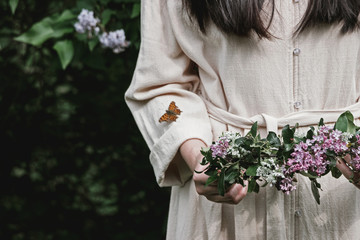 girl in linen dress holding lilac flower wreath in garden 