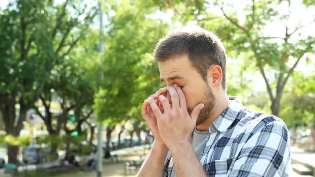 Man rubbing his eyes that sting him due to allergy or infection in a park