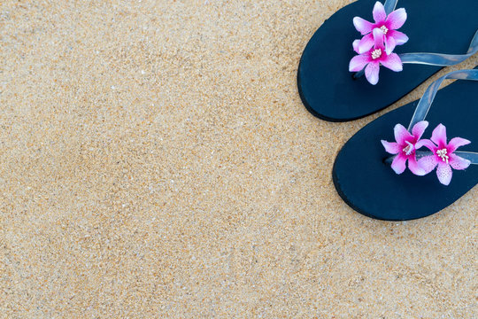 Colorful flip flops on the sandy beach.  Black slippers with a pink flower on the sand.