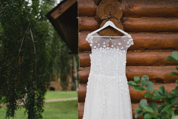 Modern bridal fashion. White wedding dress hanging on a tree outdoors in the garden.