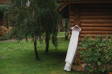 Modern bridal fashion. White wedding dress hanging on a tree outdoors in the garden.