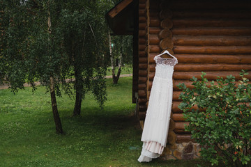 Modern bridal fashion. White wedding dress hanging on a tree outdoors in the garden.